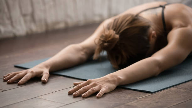 Attractive woman practicing yoga, relaxing after training, lying face down Attractive woman practicing yoga at home or in modern yoga studio with natural wooden floor, relaxing after training on mat, lying face down, beautiful sporty girl working out, close up yin yang symbol stock pictures, royalty-free photos & images