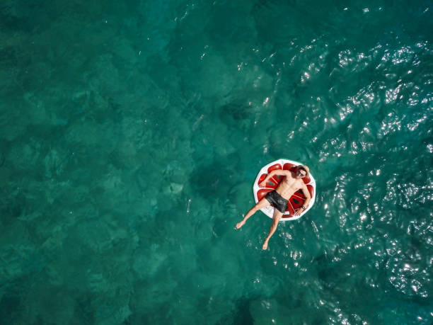 Young man relaxing on inflatable watermelon in summer on the sea stock photo