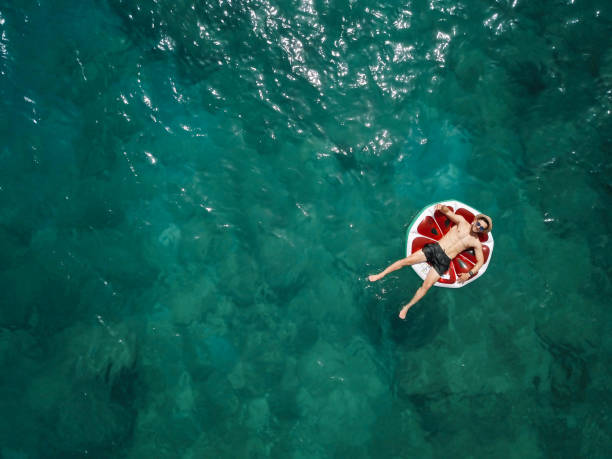 Young man relaxing on inflatable watermelon in summer on the sea stock photo