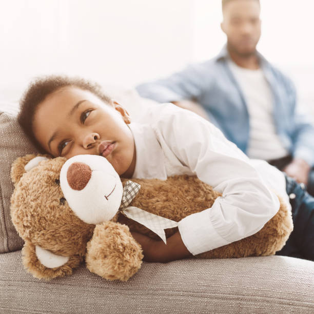 istock Sad african-american girl hugging teddy bear on sofa 1152640403