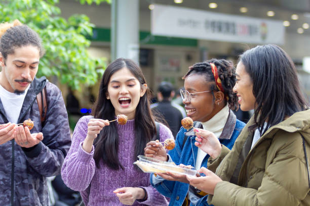Friends traveling in Japan, exploring Tokyo Friends eating Takoyaki, Japanese traditional street food, in Tokyo hot filipina women stock pictures, royalty-free photos & images