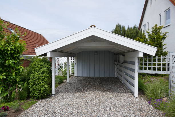 Wooden carport with pitched roof, white with open driveway on pebble floor next to a house. Germany, Europe Carport made of wood next to a house. Semi-open, white with gray back wall, pebble floor pebble driveway stock pictures, royalty-free photos & images