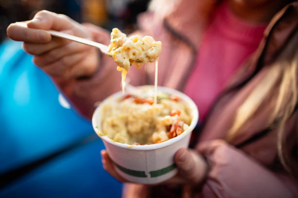 Macaroni and Cheese Street Food Close-up of an unrecognisable female adult holding a small pot of macaroni and cheese from a street food stall. convenience food stock pictures, royalty-free photos & images