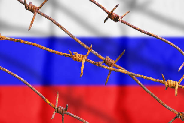 istock Russian flag behind rusty barbed wires with shadows 1152647597