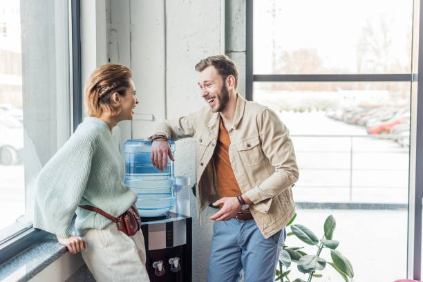 hombre de negocios casual y mujer hablando y riendo en la oficina del desván - refrigeradora de agua fotografías e imágenes de stock
