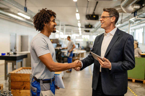 Happy engineer greeting African American worker in industrial building.
