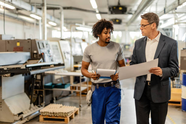 istock Company manager and black manual worker talking while analyzing project plans in a factory. 1152653292