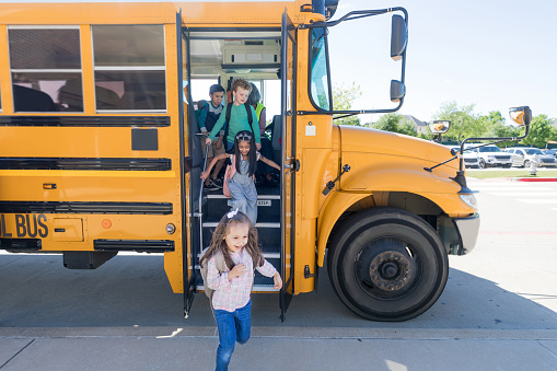 A group of elementary school children exit bus at the end of the school day.
