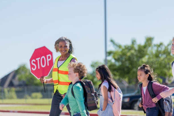 cruzar guardia lleva a los estudiantes al otro lado de la calle - crossing guard fotografías e imágenes de stock