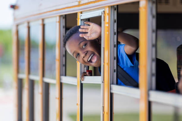 Adorable little boy waves from school bus Happy elementary age African American schoolboy smiles as he waves from a school bus. kid waves stock pictures, royalty-free photos & images