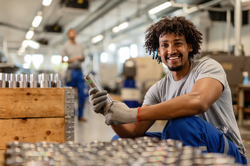 Happy black steelworker inspecting finished products in a factory and looking at camera.