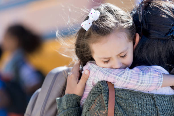 Sad little girl is apprehensive about the first day of school Worried little girl hugs her mom on the first day of school. A school bus is in the background. first day of school stock pictures, royalty-free photos & images