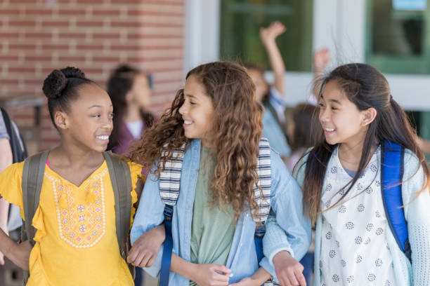 Girls walk home from school arm in arm Three junior high female friends walk out of the school building arm in arm and talking together. junior high stock pictures, royalty-free photos & images