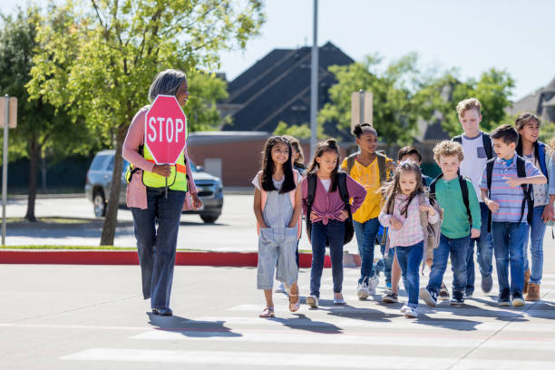 la guardia cruza femenina conduce a los niños de forma segura cruzando la calle - crossing guard fotografías e imágenes de stock