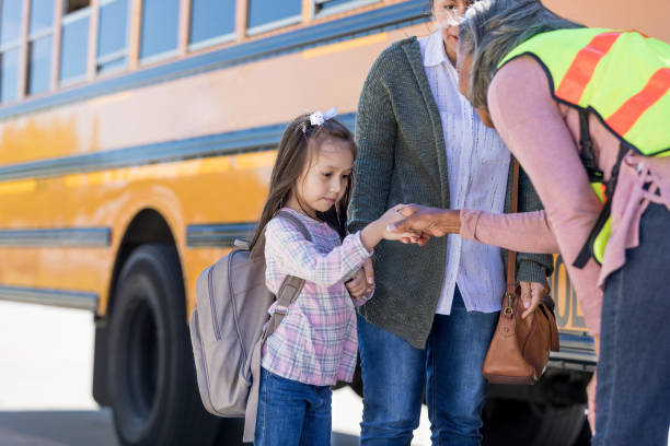 A school bus driver shakes hands with shy schoolgirl At the school bus stop, a shy schoolgirl looks down at the ground as the school bus driver leans down to shake her hand. shy stock pictures, royalty-free photos & images