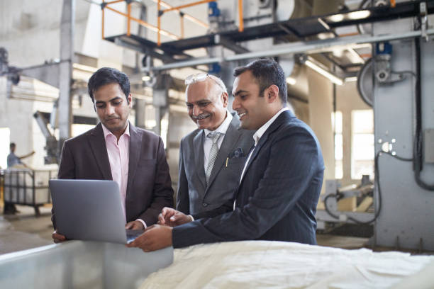 Smiling Indian Executives Meet on the Factory Floor Indian CEO and senior managers meet on the factory floor to examine manufacturing methods and ensure quality control. business stock pictures, royalty-free photos & images