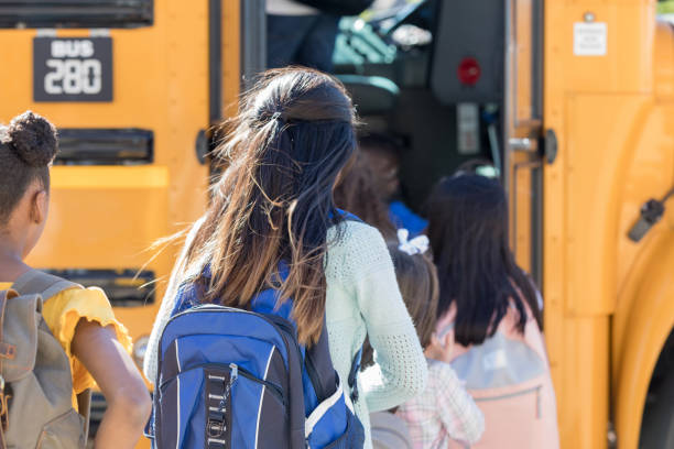 Children board a school bus in a line A line of school children with obscured faces board a school bus on their way to school. obscured face stock pictures, royalty-free photos & images