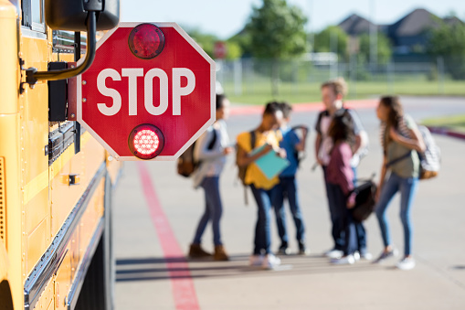 Before getting inside the school bus, a group of junior high school students stand near the bus and talk together.