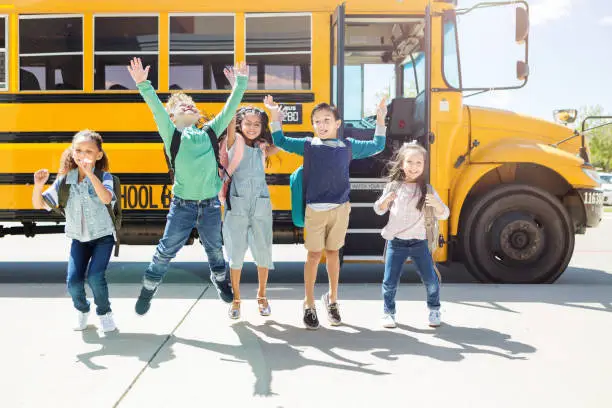 Photo of Elementary students jump for joy at bus stop