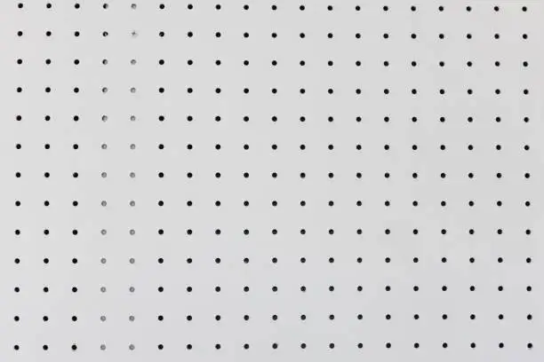orderly holes or dot rows and columns on white pegboard wall.