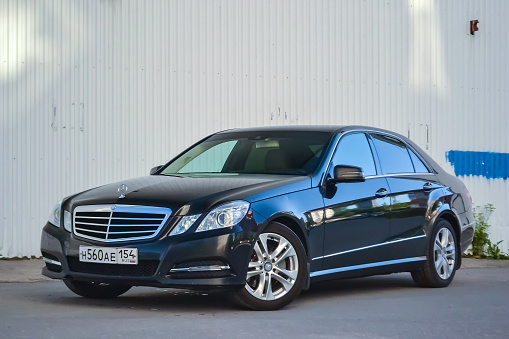 Novosibirsk, Russia - 05.30.2019: Black Mercedes Benz E-class E350 2010 year front view with dark gray interior in excellent condition in a parking space with gray wall background