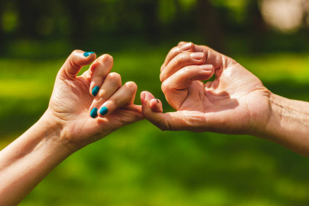 Young and mature hand making pinkie promise sign Closeup shot of hands making a pinkie promise sign in nature – Mother and daughter crossing their little fingers in symbol of commitment pinky finger stock pictures, royalty-free photos & images