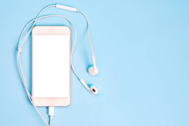 White smartphone on the blue background with headphones. View from above. White smartphone on the blue background with headphones. View from above in ear headphones stock pictures, royalty-free photos & images