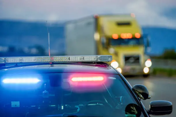 Photo of A Highway Patrol Car With The Lights On, Pulling A Driver Over For Speeding As A Semi Truck Drives Passed