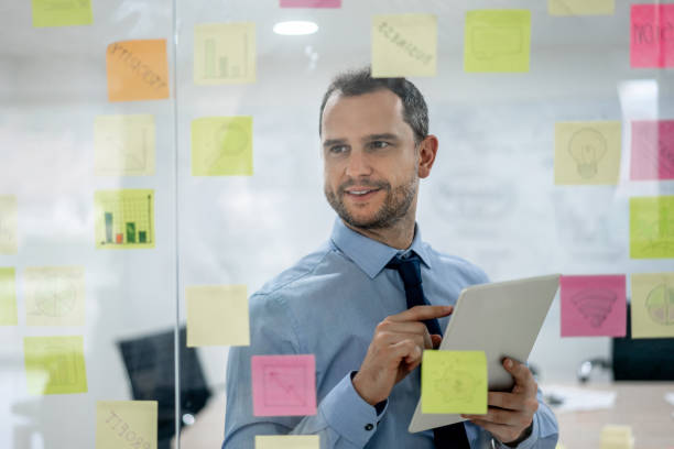istock Latin american business man using a tablet and brainstorming ideas with adhesive notes on window 1152667919