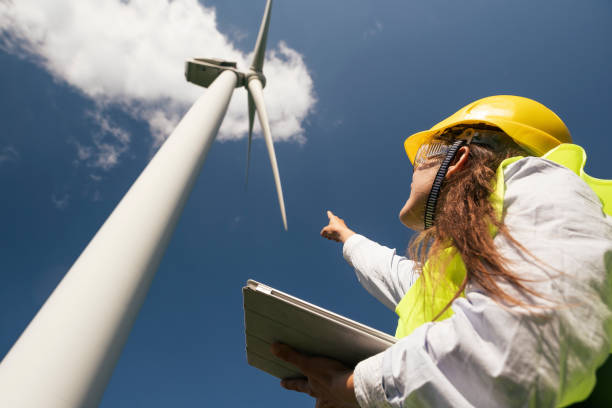 istock Renewable Energy Systems Engineering in a Wind Turbines Farm. Electricity  Maintenance Engineers working on the field near Wind Turbine Power station with a Clear Blue Sky Behind them. 1152668913