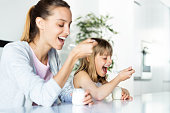 Beautiful young mother and her daughter eating iogurt at home.