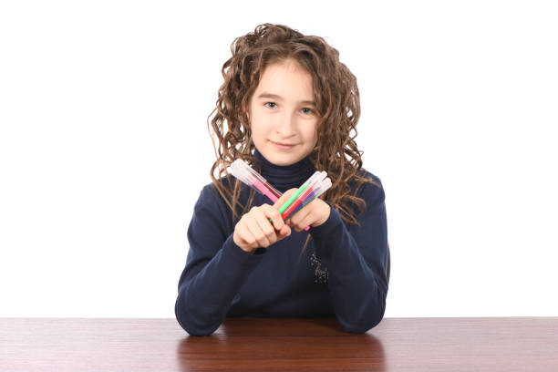 Young schoolgirl draws with markers while sitting at table, isolated over white. The concept of development of the child, the child's upbringing
