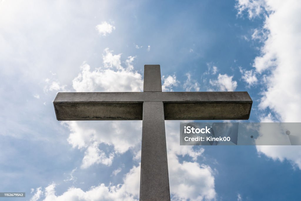 A large concrete cross on a cemetery against a blue sky with white clouds. Blue Stock Photo