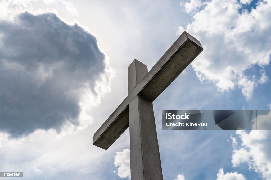 A large concrete cross on a cemetery against a blue sky with white clouds. Blue Stock Photo