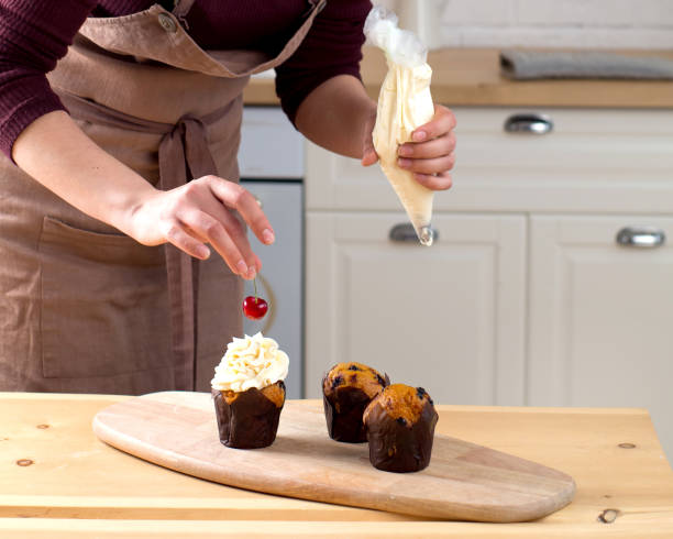 Female baker decorating cupcake with cherry and creme