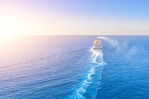 Cruise ship liner goes into horizon the blue sea leaving a plume on the surface of the water seascape during sunset. Aerial view, concept of sea travel, cruises.