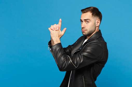 Handsome stylish young unshaven man in black leather jacket white t-shirt looking camera isolated on blue background studio portrait. People sincere emotions lifestyle concept. Mock up copy space