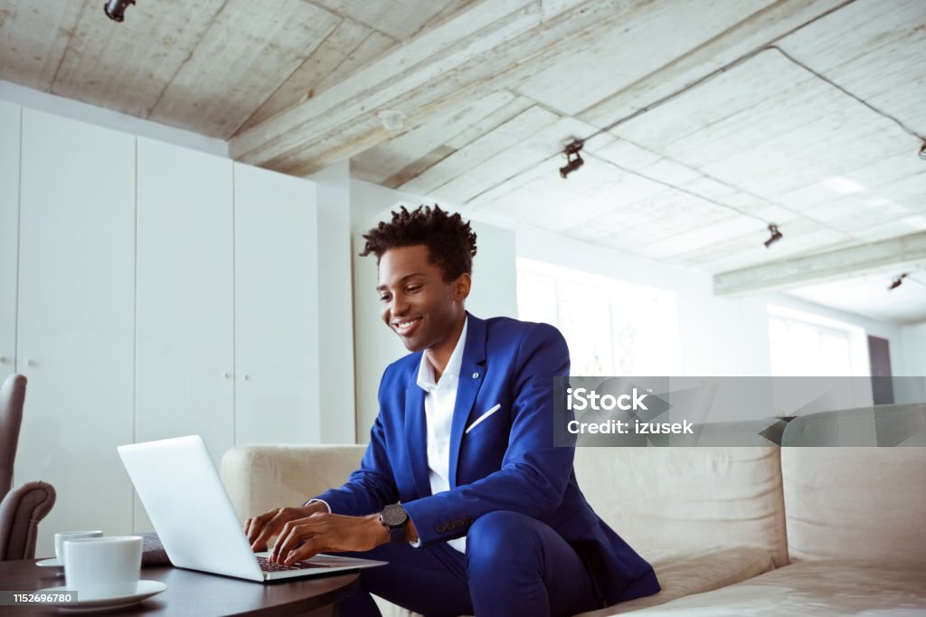 Smiling male executive working on sofa in office Smiling male executive working while sitting on sofa. Mid adult white collar worker is using laptop in office. He is related to financial occupation. 30-34 Years Stock Photo