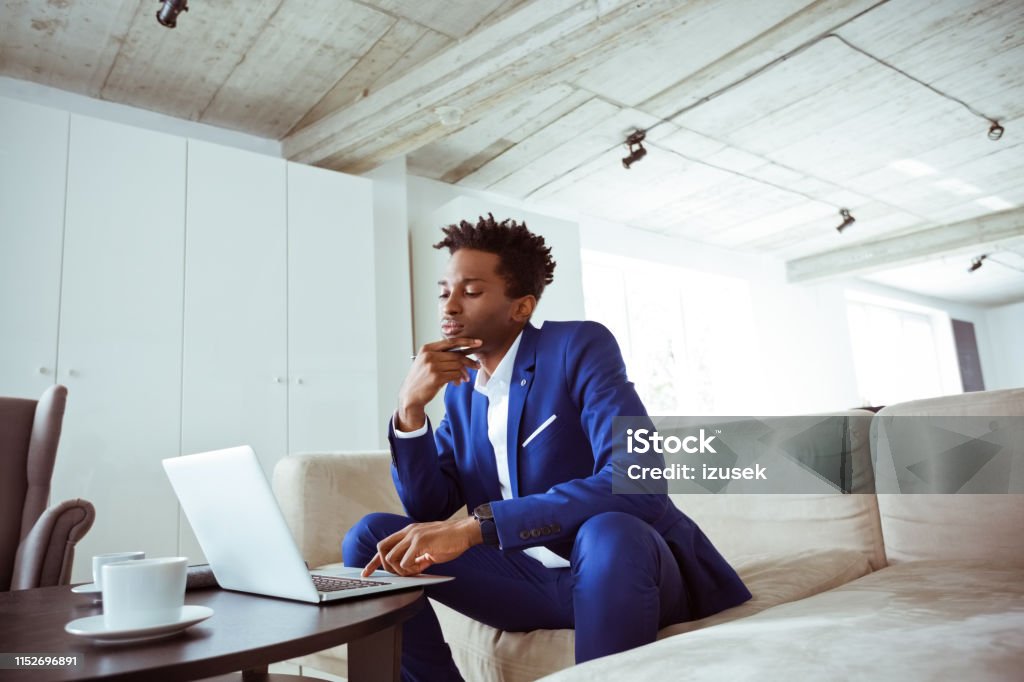 Businessman using laptop while sitting in office Thoughtful businessman using laptop while sitting in office. Financial advisor is wearing suit. He is working on financial strategies. 30-34 Years Stock Photo