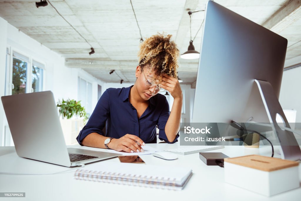 Businesswoman with headache working in office Tired businesswoman having headache at creative workplace. Female financial expert is sitting with head in hands at desk. She is working in office. 30-34 Years Stock Photo