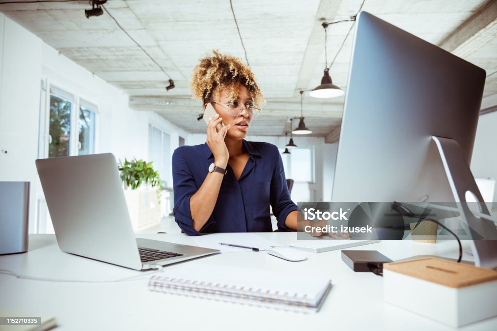 Female financial executive talking on smart phone Female financial expert talking on smart phone. Skilled business executive is using computer in office. She is working at desk. Financial Advisor Stock Photo