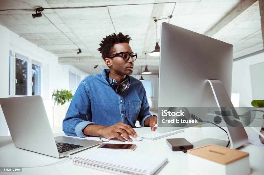 Confident financial advisor using computer at desk Male financial advisor using computer at desk. Confident businessman is sitting in workplace. He is working at creative office. African-American Ethnicity Stock Photo