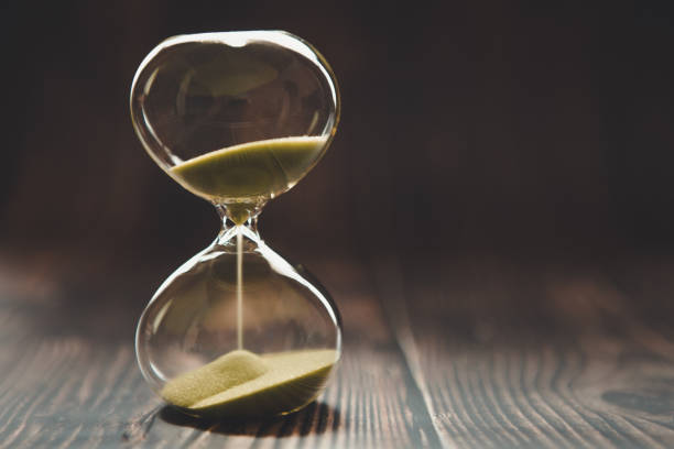 istock Hourglass with falling sand inside a glass bulb, passing time or lost time on a dark background with space for text 1152712173