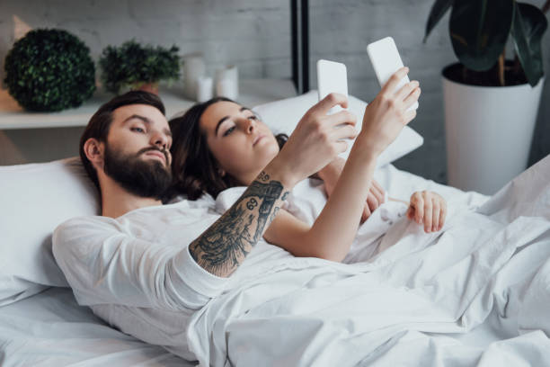 istock beautiful young couple lying in bed and using smartphones 1152713699