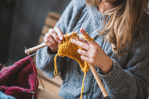 Lovely adorable caucasian grandmother knitting cardigan on her leisure time sitting on sofa in glasses, recollecting good memories, thinking of her life with smile, enjoying peaceful moment