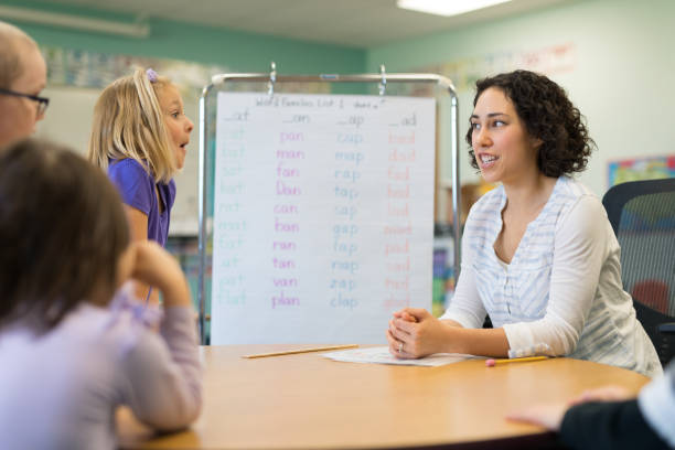 istock Female teacher sitting with first grade students at a classroom table 1152726175