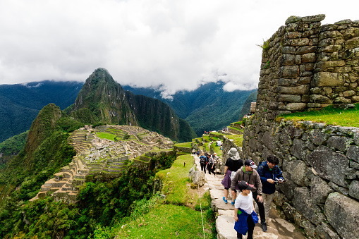 Machu Picchu, Peru - February 12, 2018: Asian family walks through the ruins of Machu Picchu while taking photos with a cell phone
