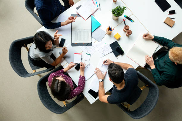 Business group working together on new project Top view shot of business colleagues discussing over a new project in office. Group of young men and woman brainstorming around table while working on new project. market research stock pictures, royalty-free photos & images