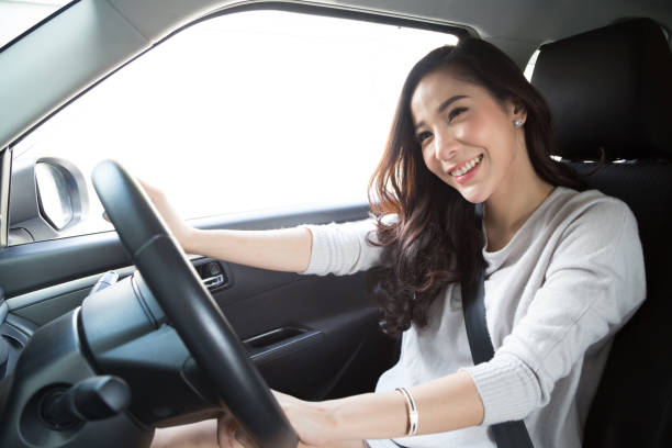 mulher asiática nova que conduz seu carro e prende a correia de assento com expressão positiva feliz durante a movimentação à viagem, mulher feliz do sorriso relaxed no conceito das férias da viagem de estrada - wayfaring - fotografias e filmes do acervo