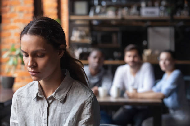 Upset mixed race woman suffering from bullying, sitting alone in cafe Upset mixed race woman suffering from bullying, discrimination, excluded girl having problem with bad friends, feeling offended and hurt, sitting alone in cafe, avoiding people, social outcast indifference stock pictures, royalty-free photos & images